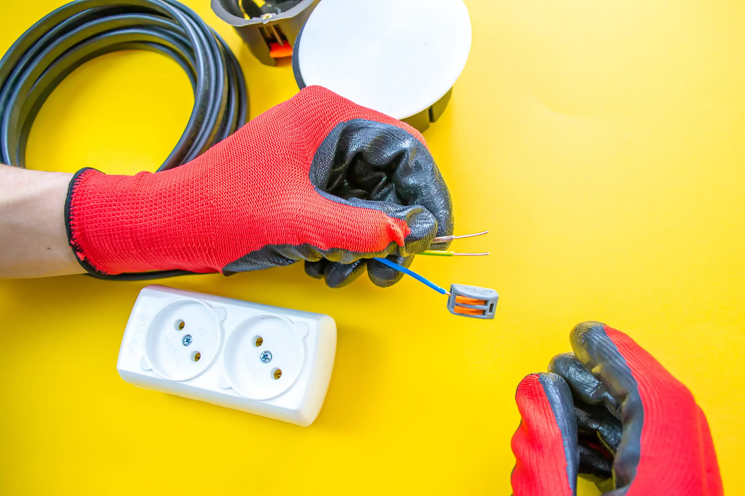 Pracownik wykonujący instalację elektryczną, trzymający przewody w rękawicach ochronnych