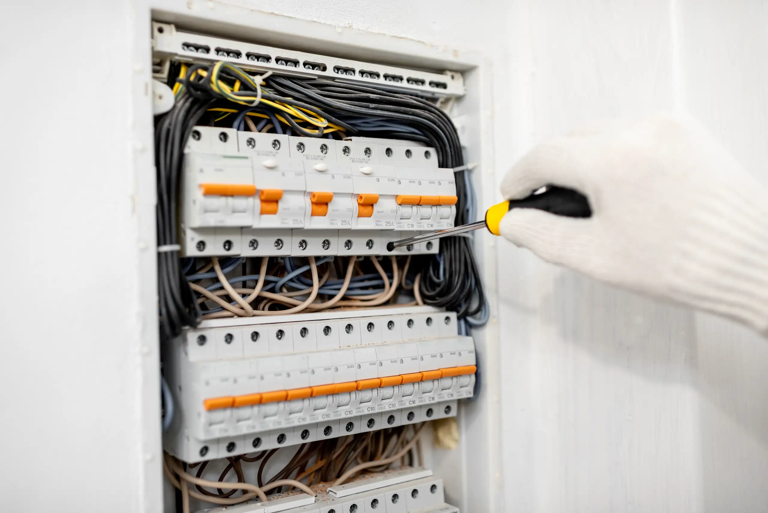 Montaż instalacji elektrycznej w rozdzielni, z widoczną ręką technika i narzędziem
